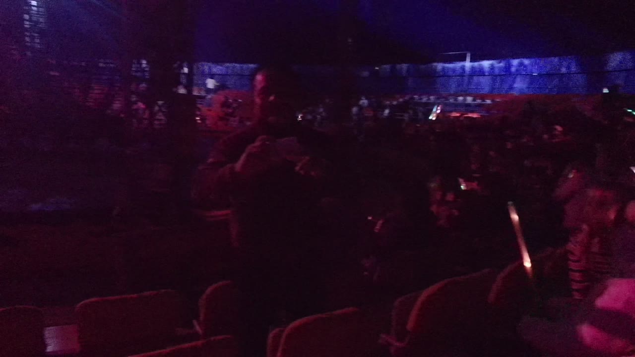Audience members seated in a dark venue with colored light.