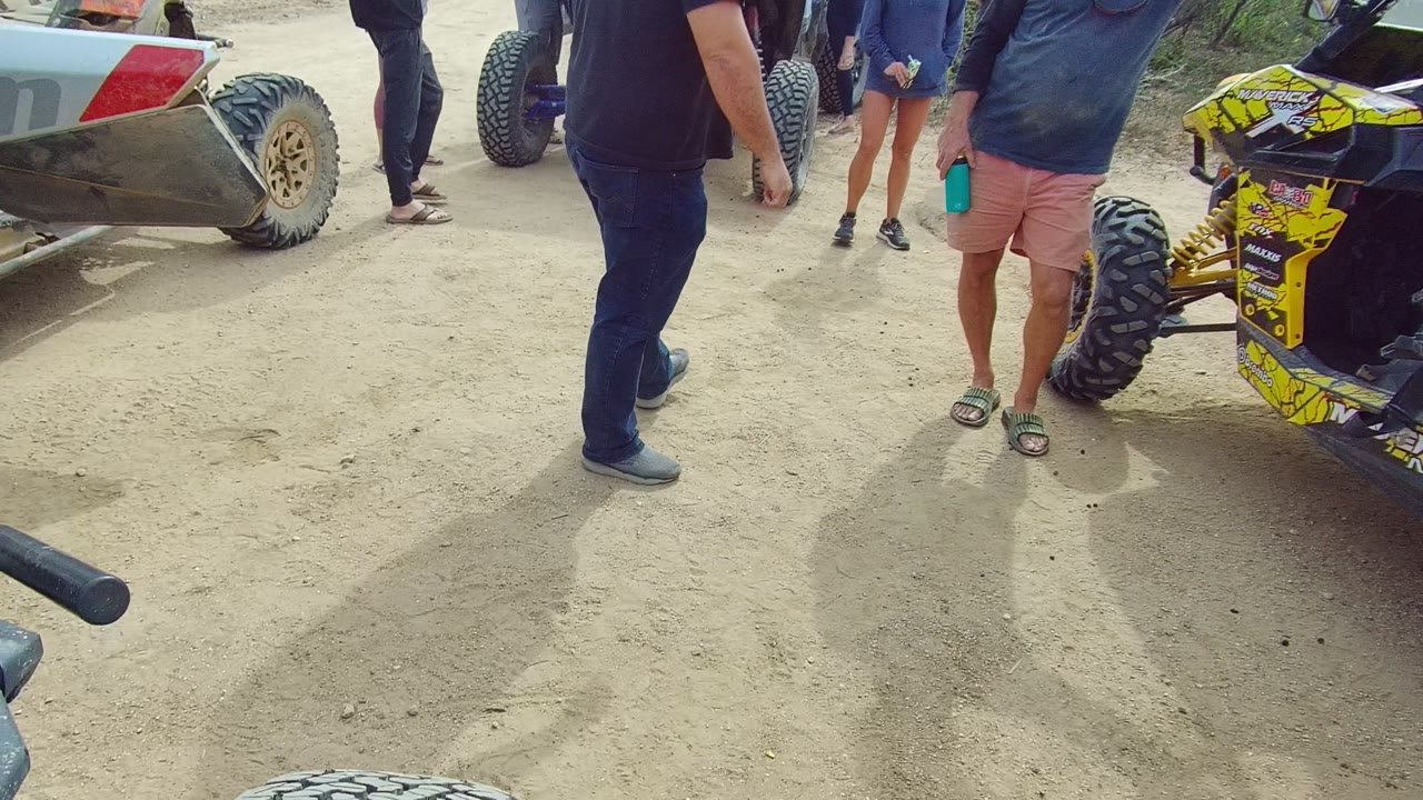 People standing near a black and red off-road vehicle on dusty ground.