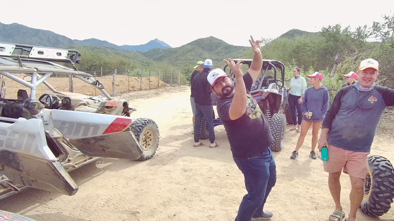 People stand near off-road vehicles on a dirt road in desert hills.