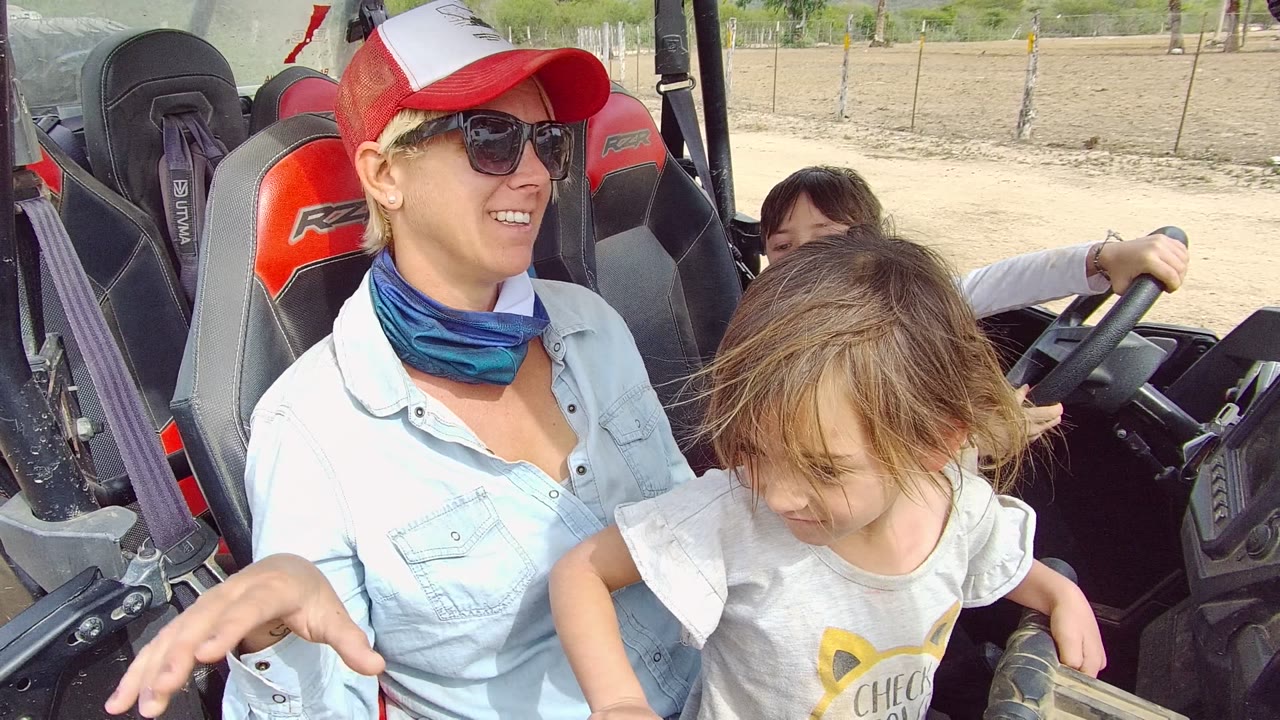 Woman and two children inside an off-road vehicle with dry terrain behind them.