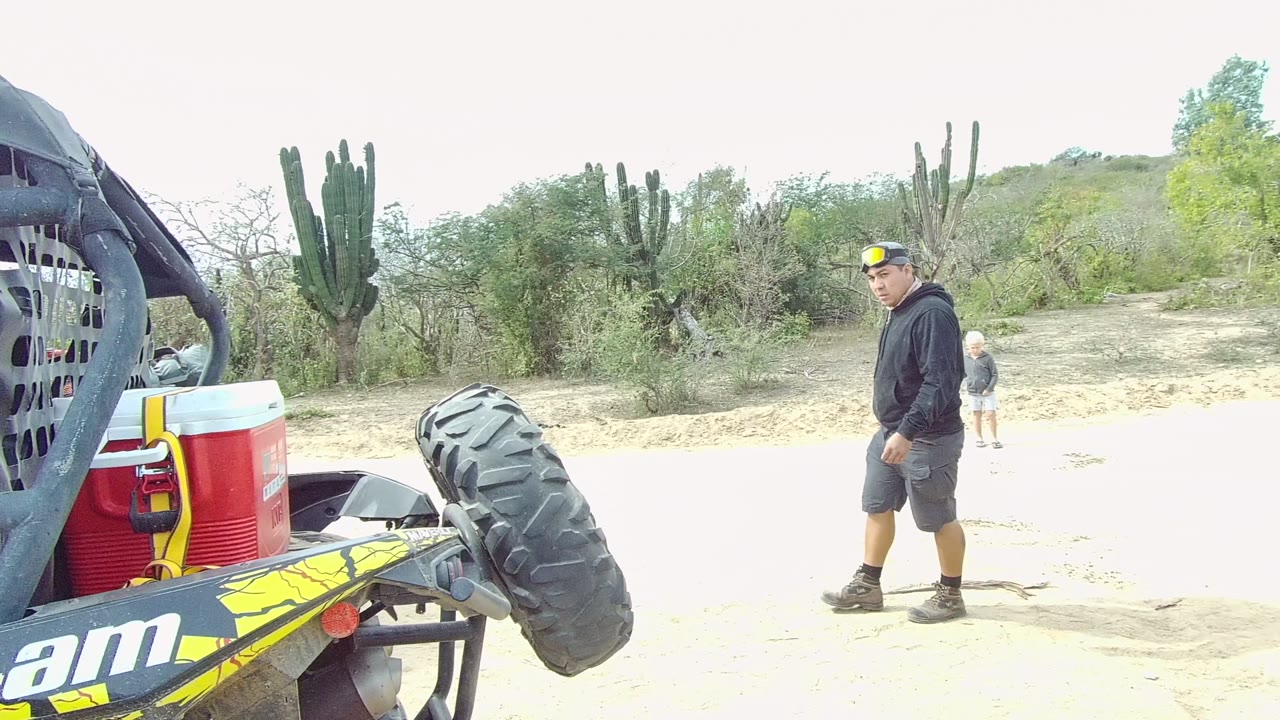 Can-Am buggy rear beside adults walking on a sandy desert road.