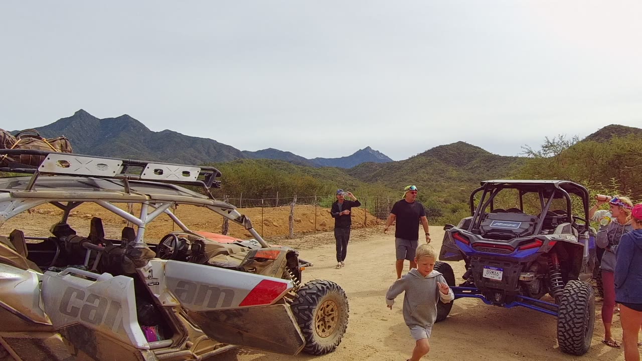 Child walking past a silver off-road vehicle in desert terrain