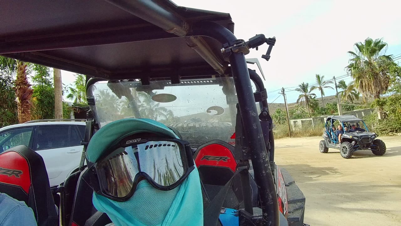 Rider framed low inside a UTV with buggies visible on the road ahead.