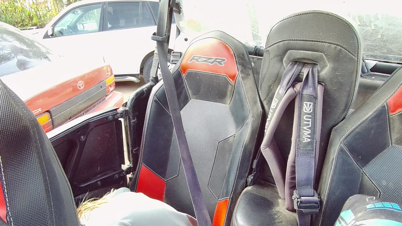 Close view of RZR seats and harnesses with parked cars behind