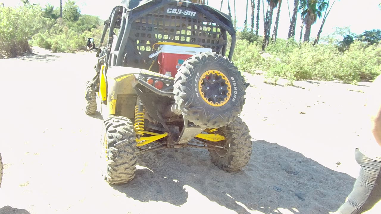 Parked UTV on sandy ground with a partial person at the right edge.