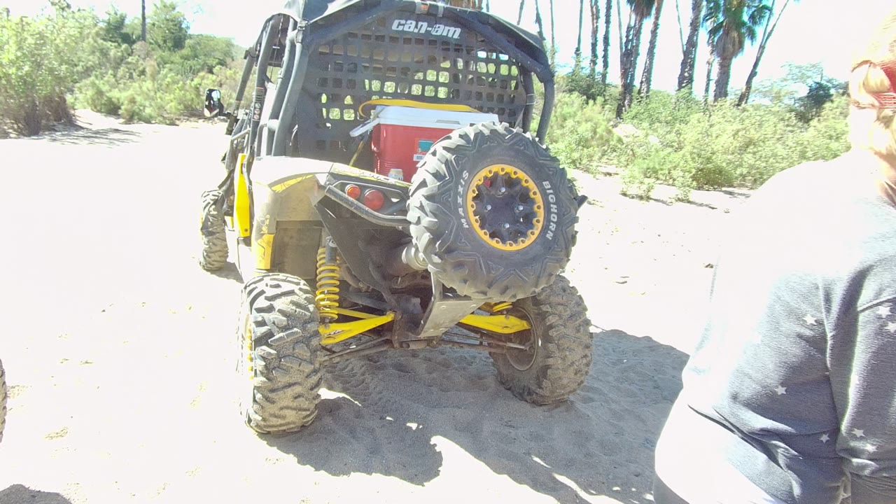 The rear of the yellow and black off-road vehicle fills the left side of the Los Cabos frame while a person in a gray top is cropped at the right edge.