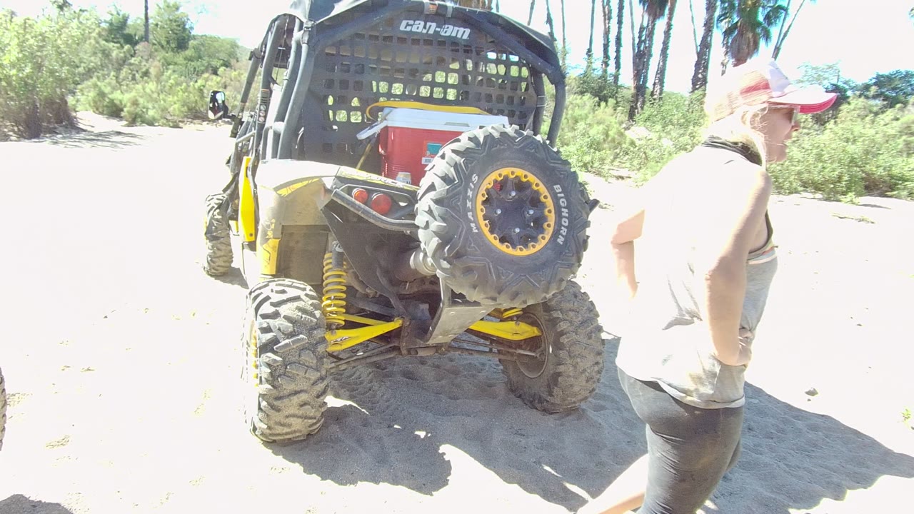 Rear view of a yellow-accented off-road vehicle in Los Cabos, Baja California Sur, with a person in a cap partly visible at the right edge beside bright sandy ground.