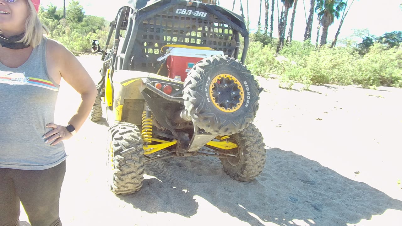 Parked off-road vehicle with a woman cropped at left on sandy terrain.