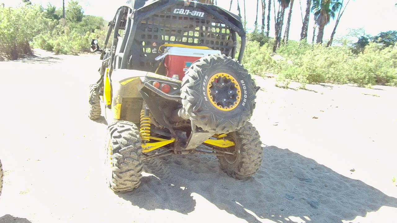 Rear of a yellow off-road vehicle on sand under bright sun.