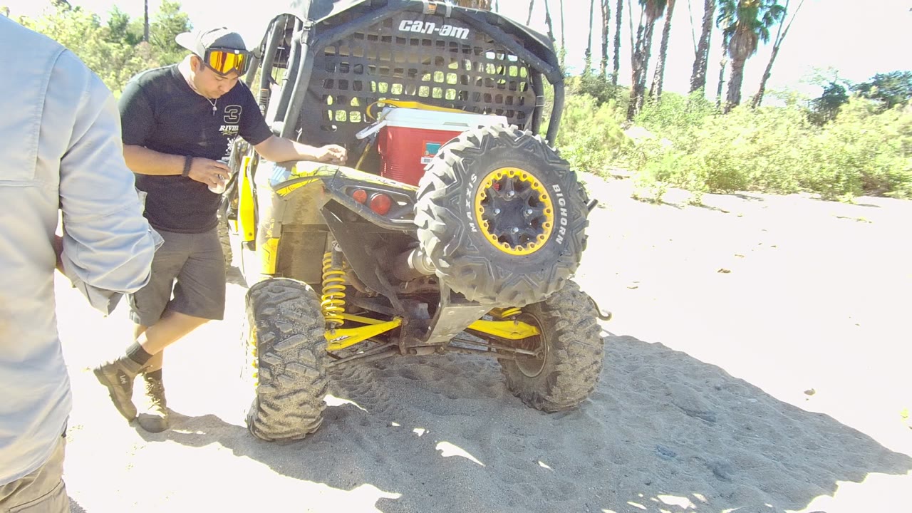 In Los Cabos, Baja California Sur, the man is closer to the ATV side with one hand near the vehicle, while the large rear tire and bright yellow suspension dominate the frame.