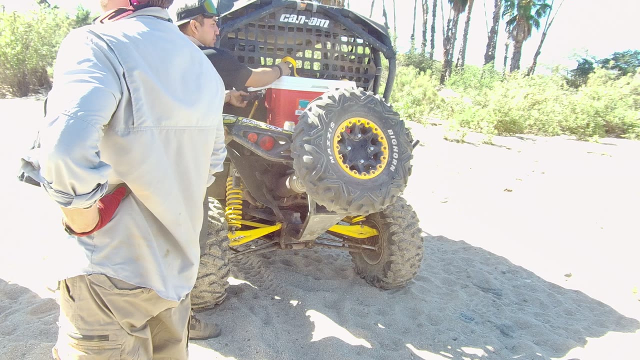 Man in a light shirt stands near a red utility vehicle while another man reaches toward it.