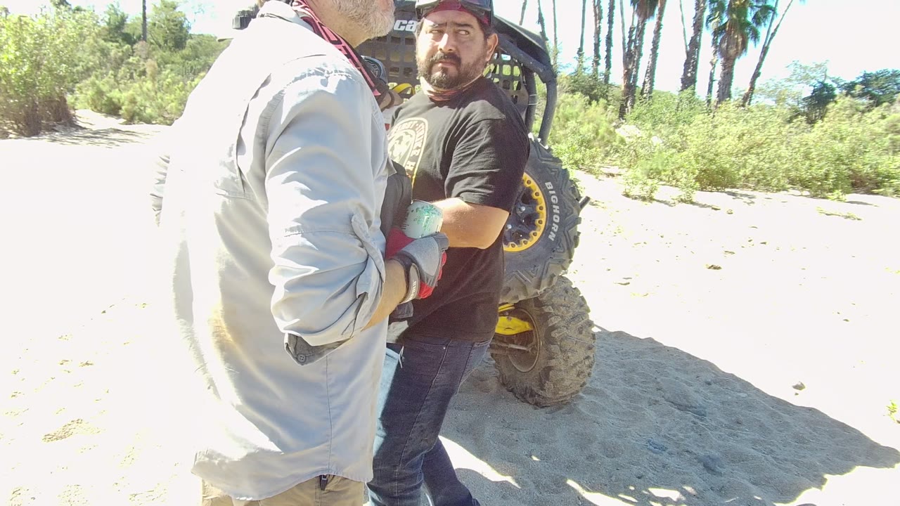 Man in a black shirt faces another man near the off-road vehicle.