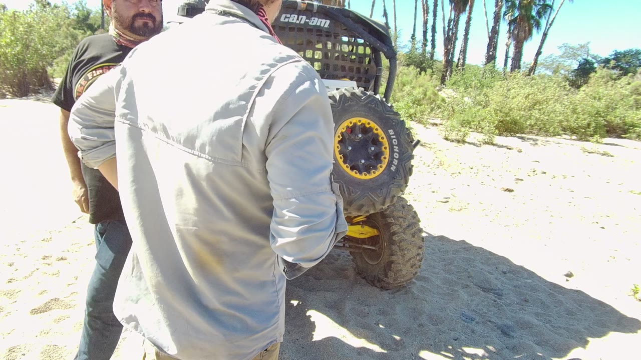 In Los Cabos, Baja California Sur, the gray-shirted man turns his back toward the camera while the black-shirted man stands near the off-road vehicle.