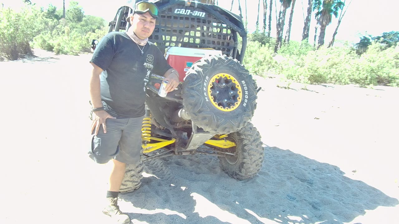 Man beside an off-road vehicle with bright sand and greenery behind him.