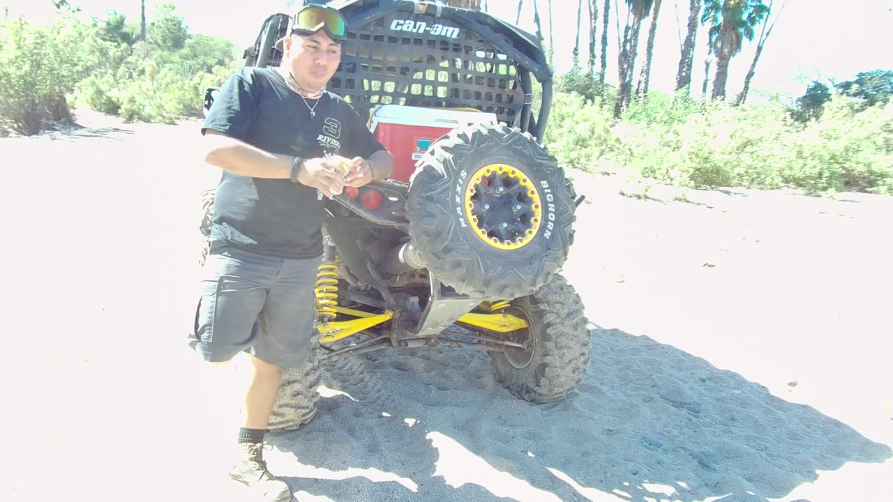 Man holding a bottle beside the rear tire of an ATV.