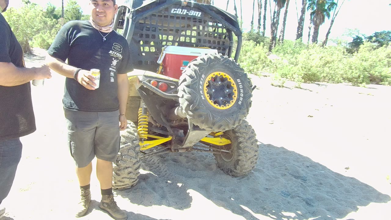 Man holding a drink near a dune buggy with a spare tire.