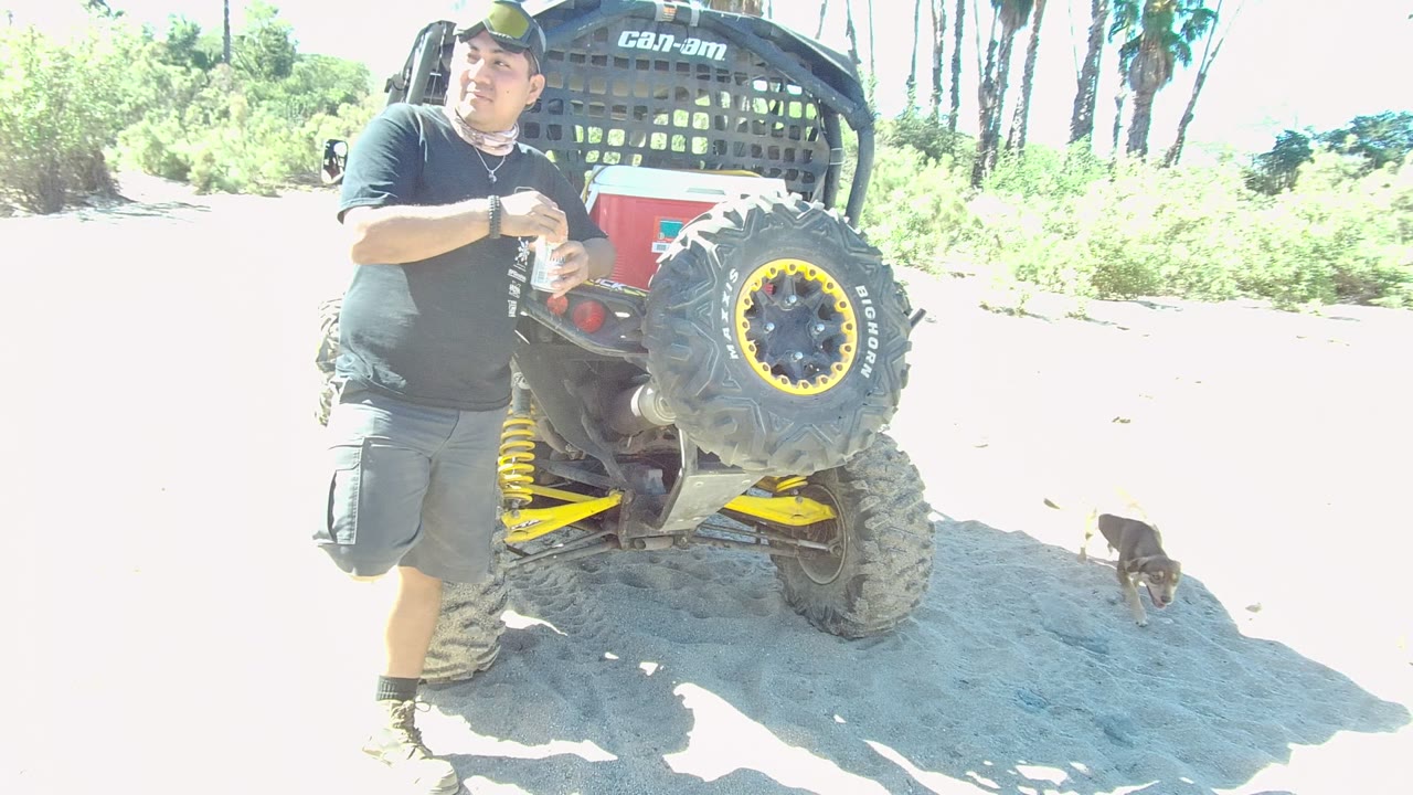 Man beside ATV as a small dog appears on the sandy ground behind him.