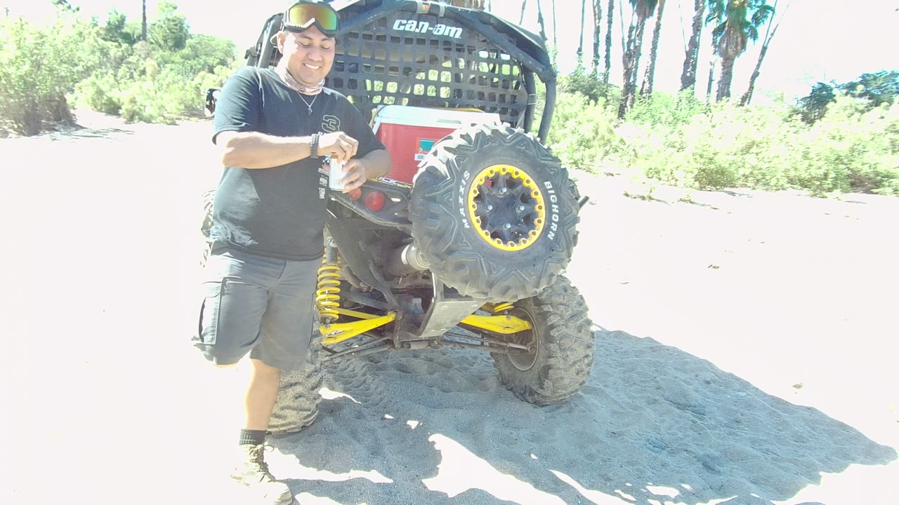 Man leaning near the rear of an ATV with yellow-rimmed tire.