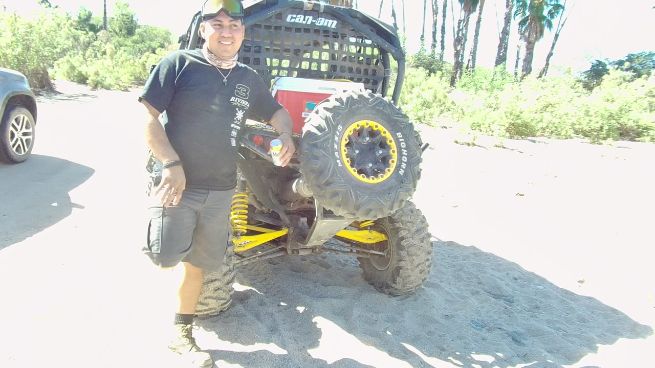 Man smiling beside the rear tire of an off-road vehicle.