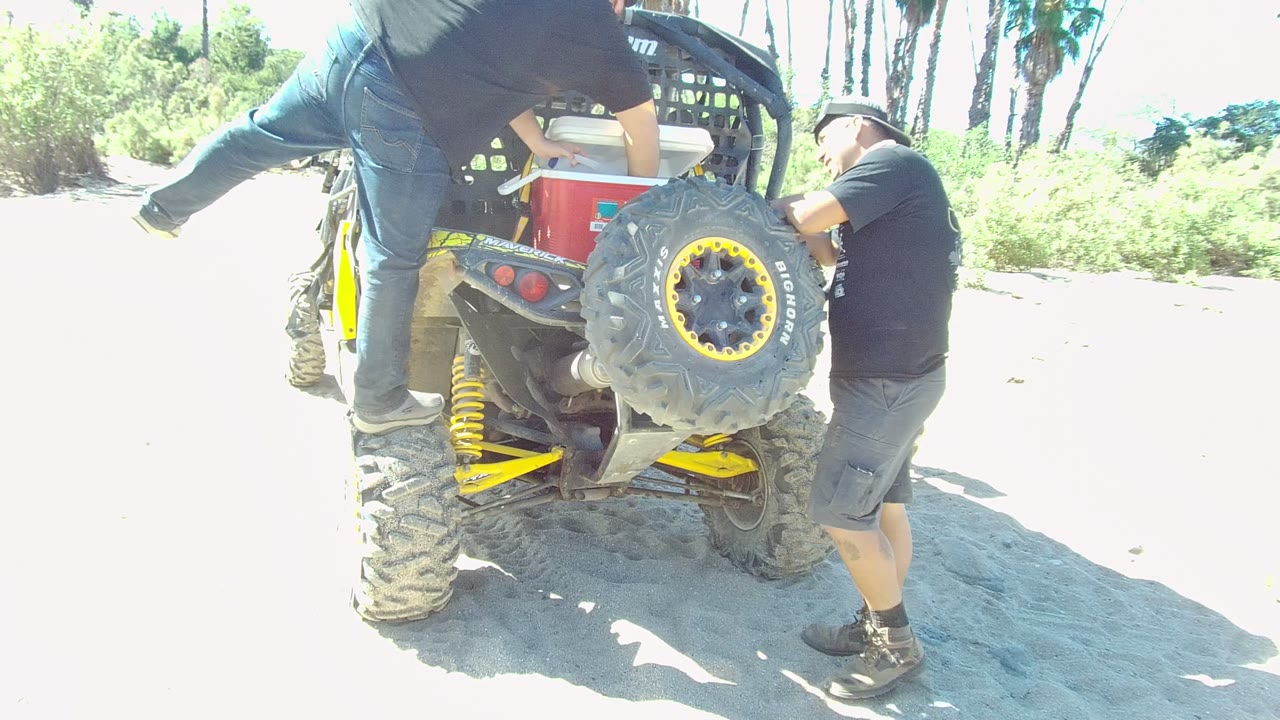 Man balanced on the ATV as another man grips the rear side near the spare tire.