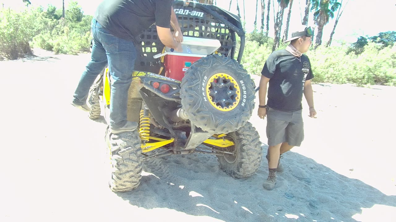 Man walking past the rear of an ATV while another stands on it.
