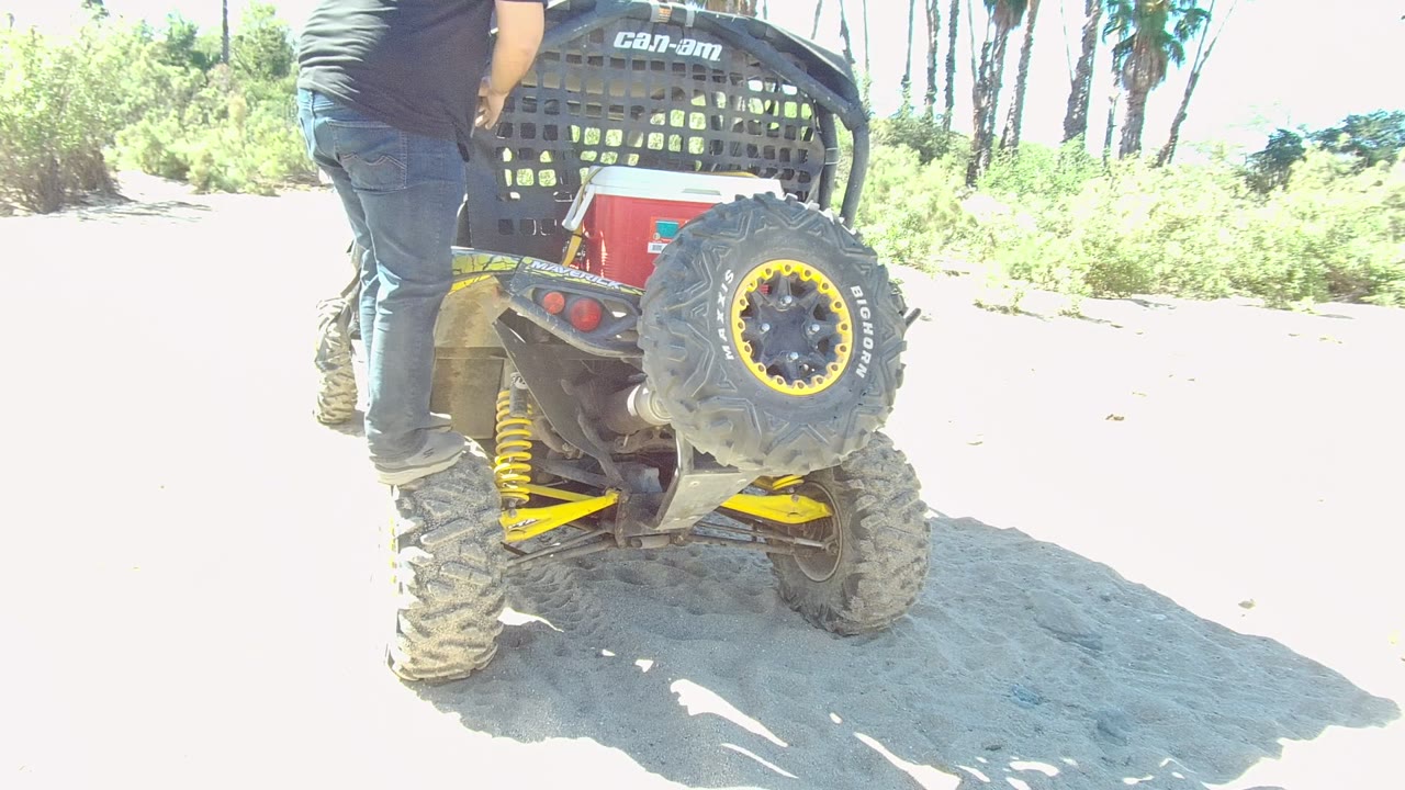 Person standing beside the rear tire of an off-road vehicle on sandy ground.