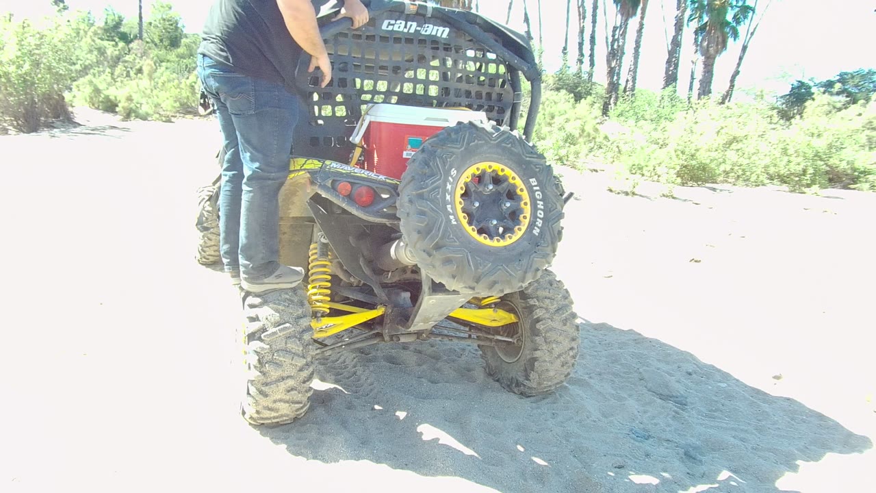 In Los Cabos, Baja California Sur, the person stands at the back of the off-road vehicle while the visible Can-Am branding, spare tire, and bright sandy path fill the frame.