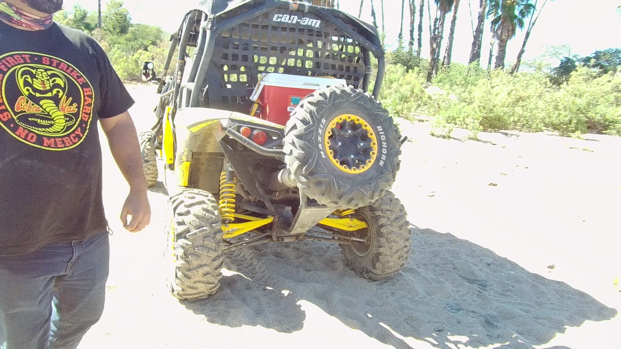 Man standing near UTV rear on bright sandy terrain.