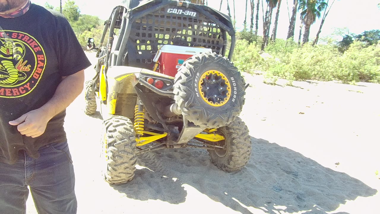 Man at frame edge with off-road vehicle and palm trees behind.