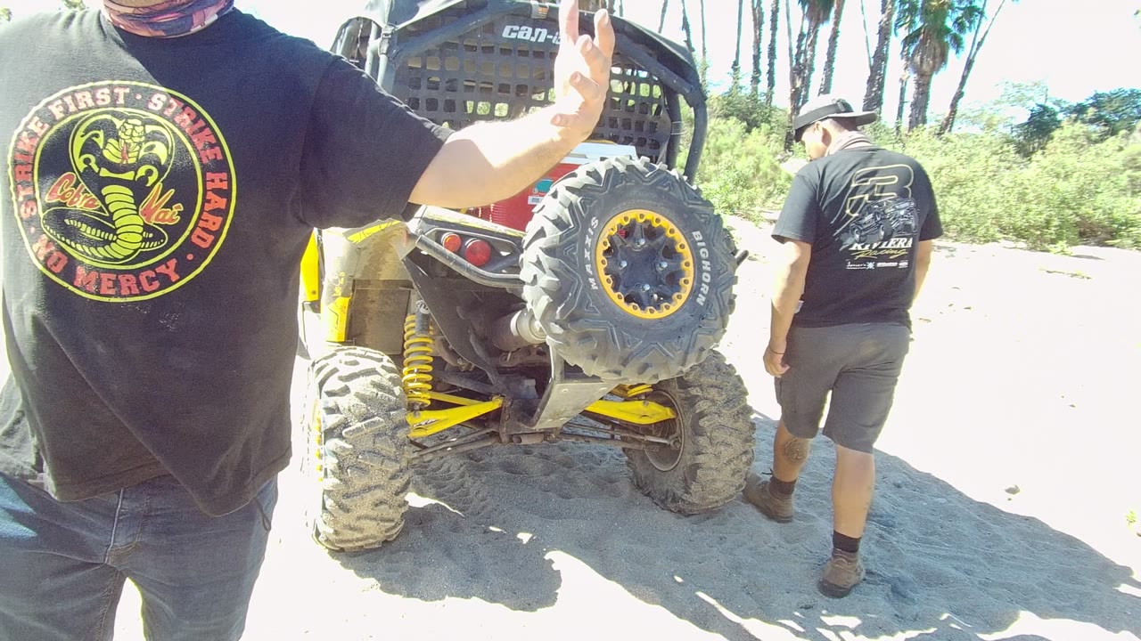 Cropped man gestures beside an off-road vehicle as another man walks away.