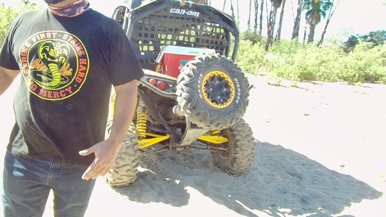 Man gestures beside the rear of a Can-Am off-road vehicle.
