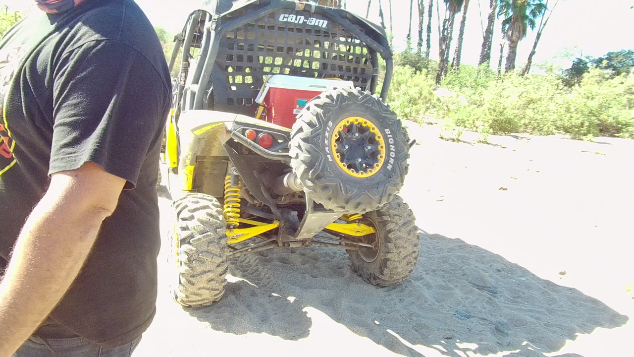 Close view of a man and the rear tire of a Can-Am off-road vehicle in bright sun.