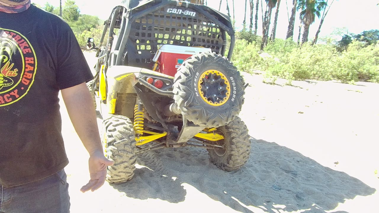 In Los Cabos, Baja California Sur, the man faces more toward camera with a neck covering visible, standing near the off-road vehicle's rear corner and tire.
