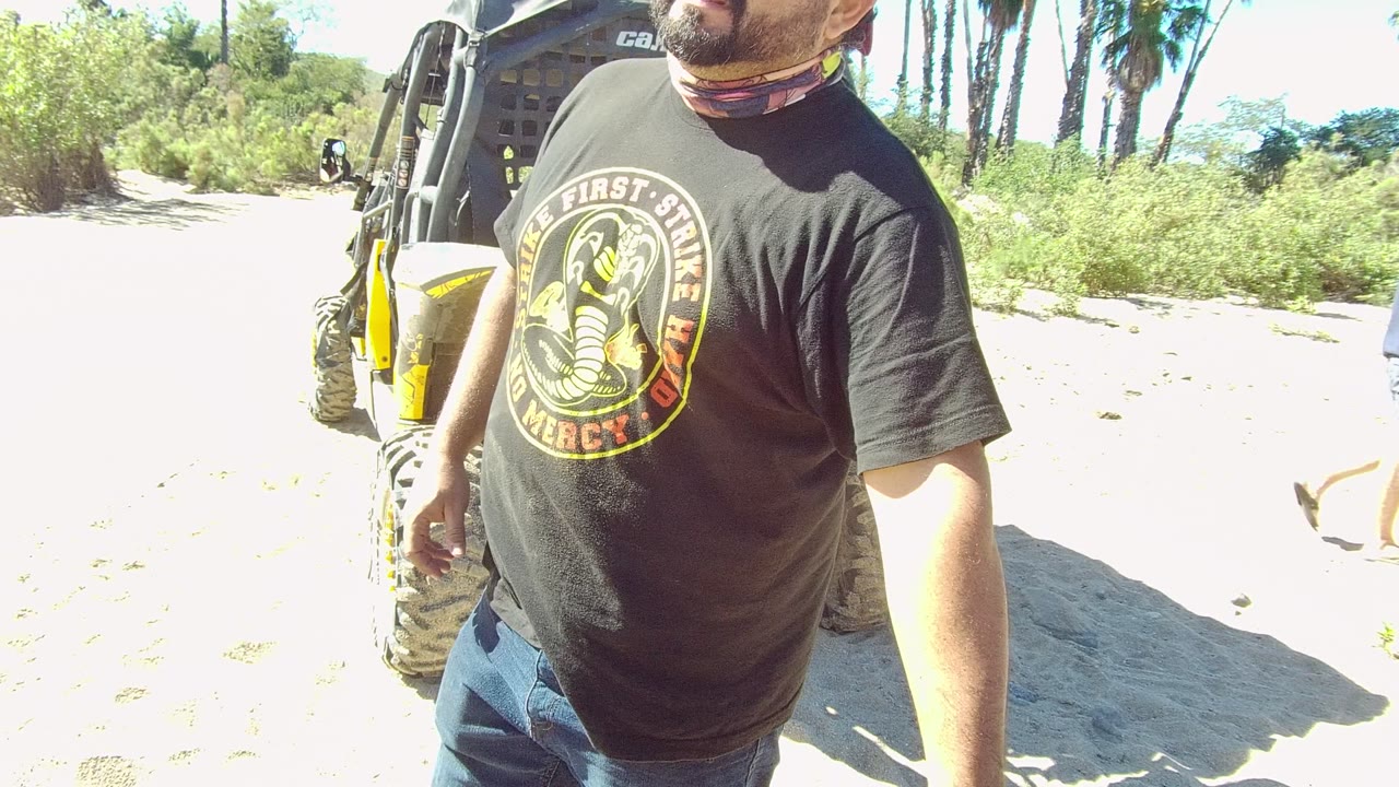 Man in black T-shirt near off-road vehicle with another person walking in the background.
