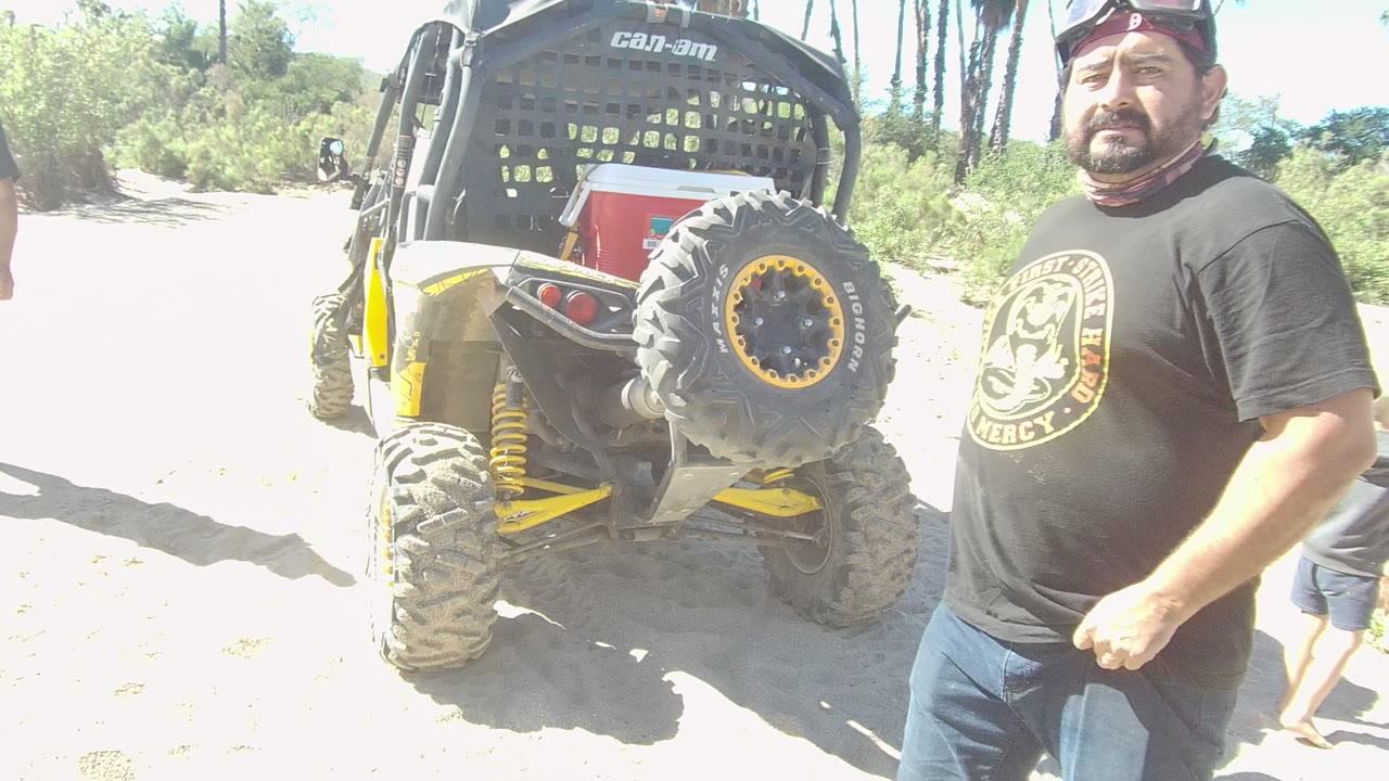 Man close to camera beside a yellow off-road vehicle on sand.