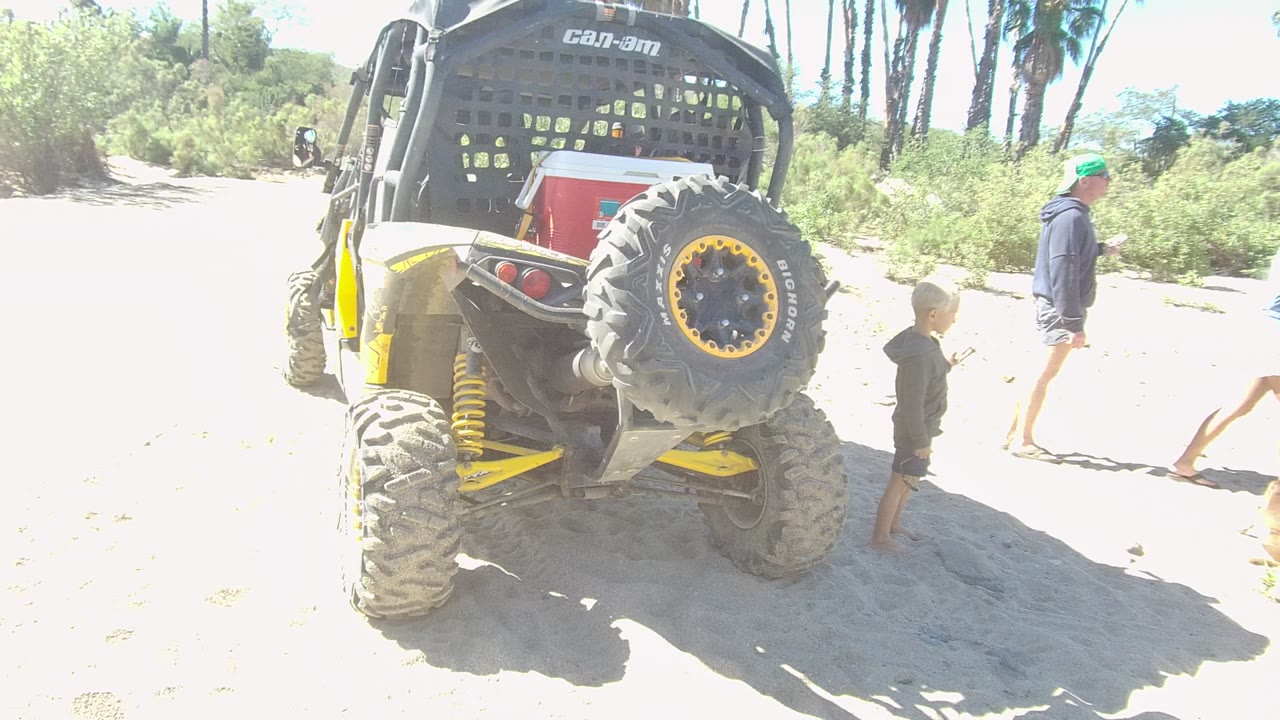 Child near dune buggy while an adult walks across sandy ground.