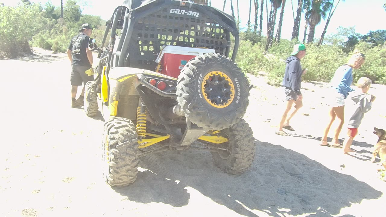 Adults and children walk beside a yellow off-road vehicle on sandy ground.