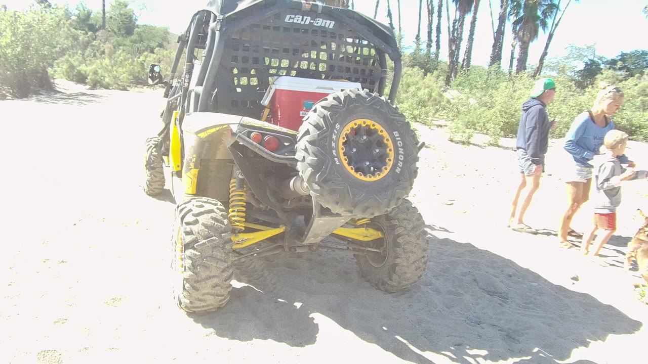 In Los Cabos, Baja California Sur, a woman bends toward a child near the right edge while the yellow Can-Am vehicle remains parked in the sandy foreground.