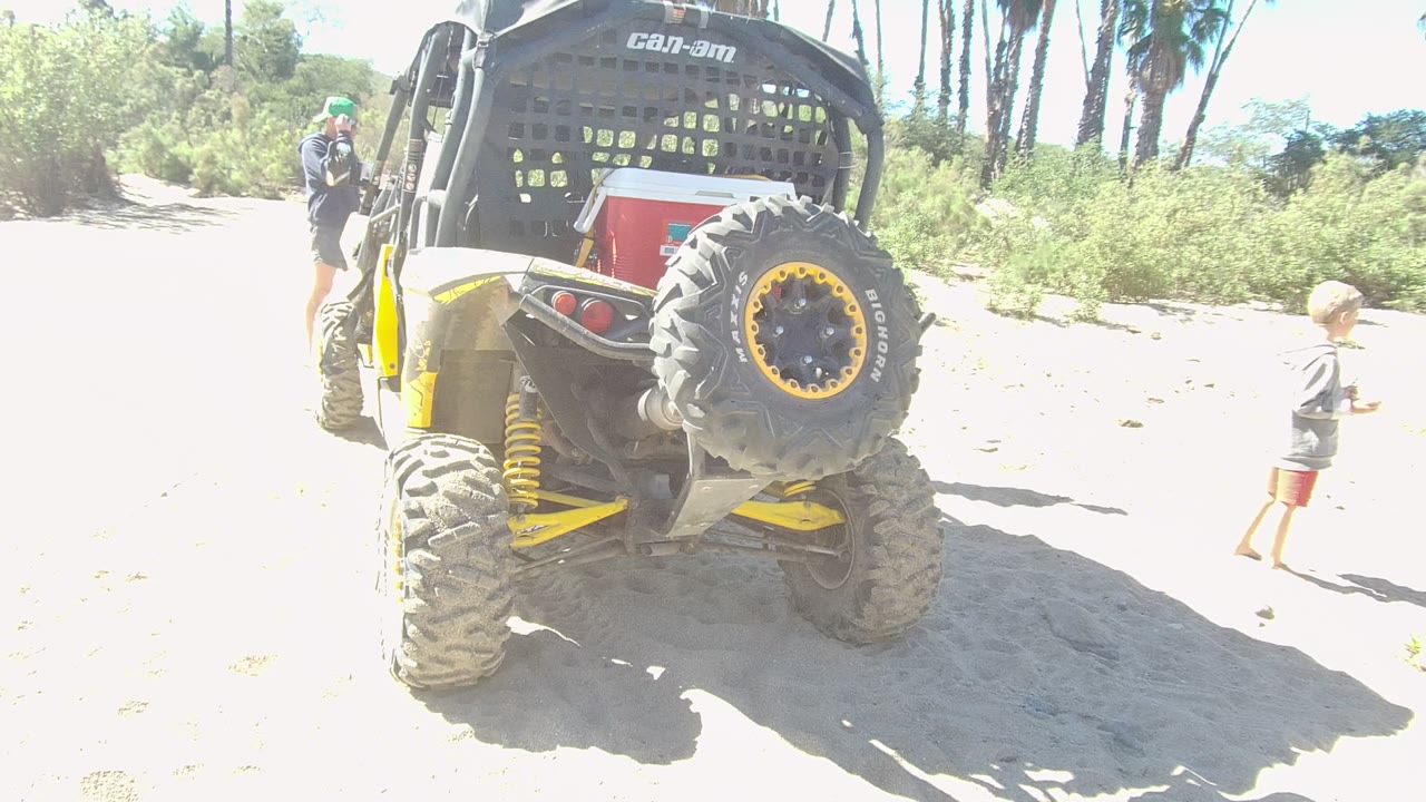 UTV rear and spare tire beside a child walking on sand.