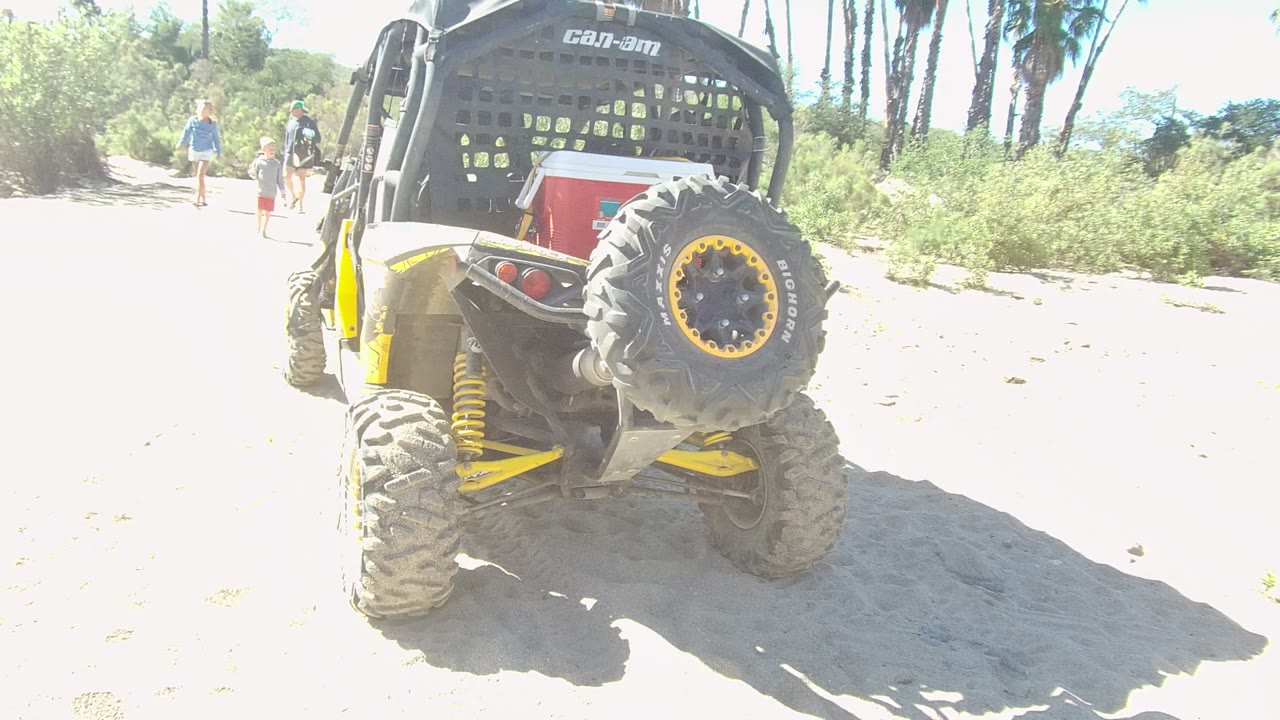 Rear of a parked UTV on sand with walkers farther down the path.