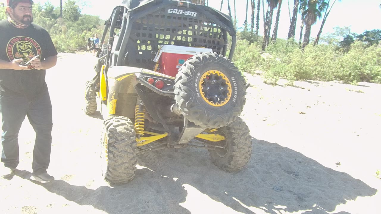 Man holding a phone next to the rear of a yellow and black off-road vehicle