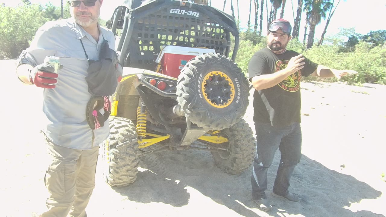 A man stands near the rear tire while another man is partly in frame beside the Can-Am.