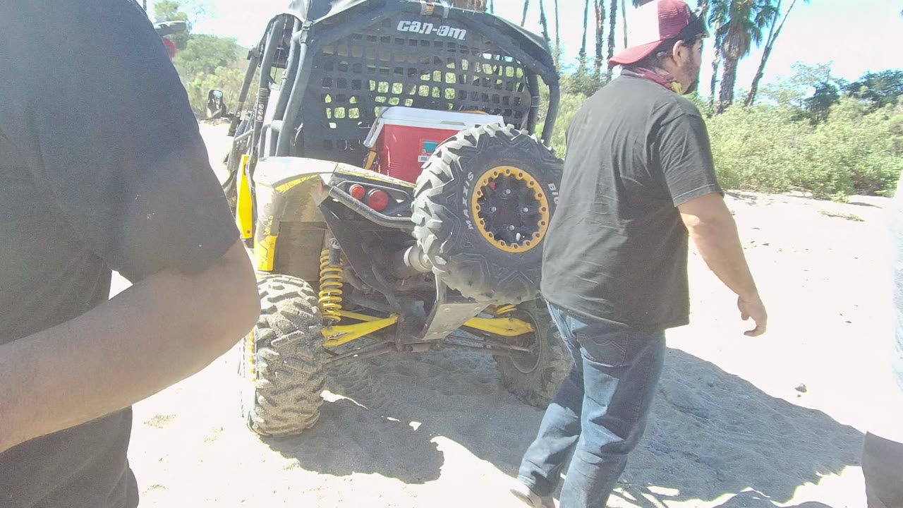 Men walking beside the rear of an off-road vehicle on sand.