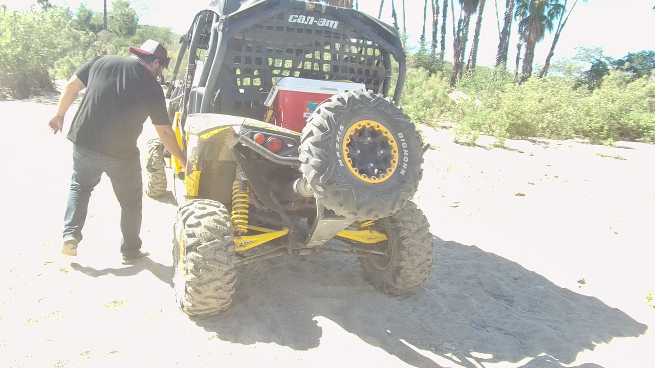 Man standing close to rear tire of yellow off-road vehicle.