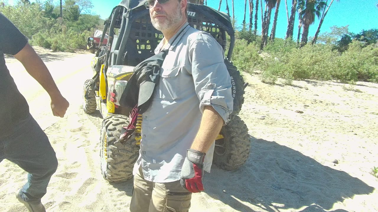 Man in light shirt near a parked off-road utility vehicle on a sandy path.