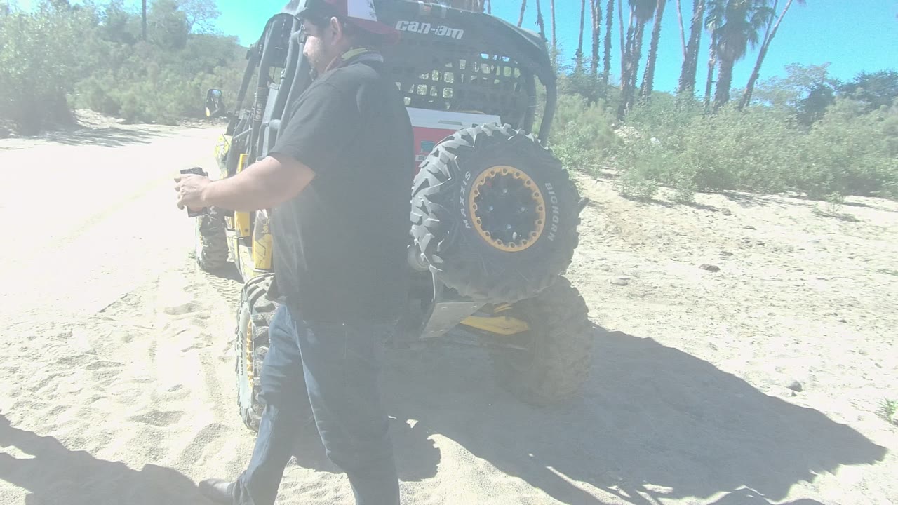 In Los Cabos, Baja California Sur, a man in a dark shirt walks past the rear of the parked dune buggy while sandy ground and desert vegetation fill the background.