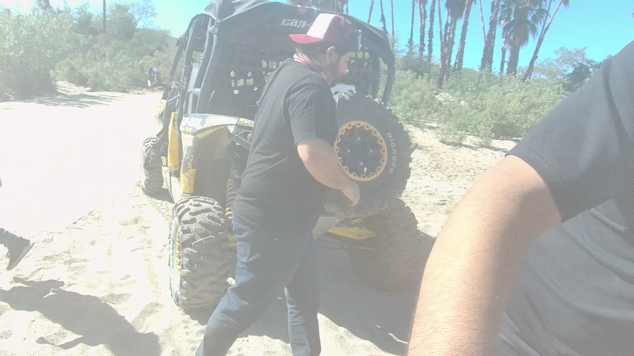 Man beside rear spare tire on an off-road vehicle in sand.
