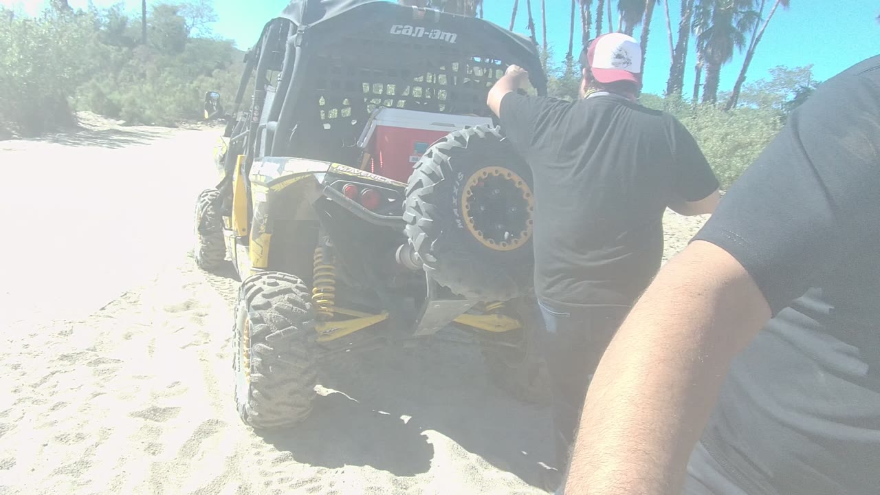 The rear of the off-road vehicle remains centered on the sandy track in Los Cabos while a man's arm and torso fill the right foreground.
