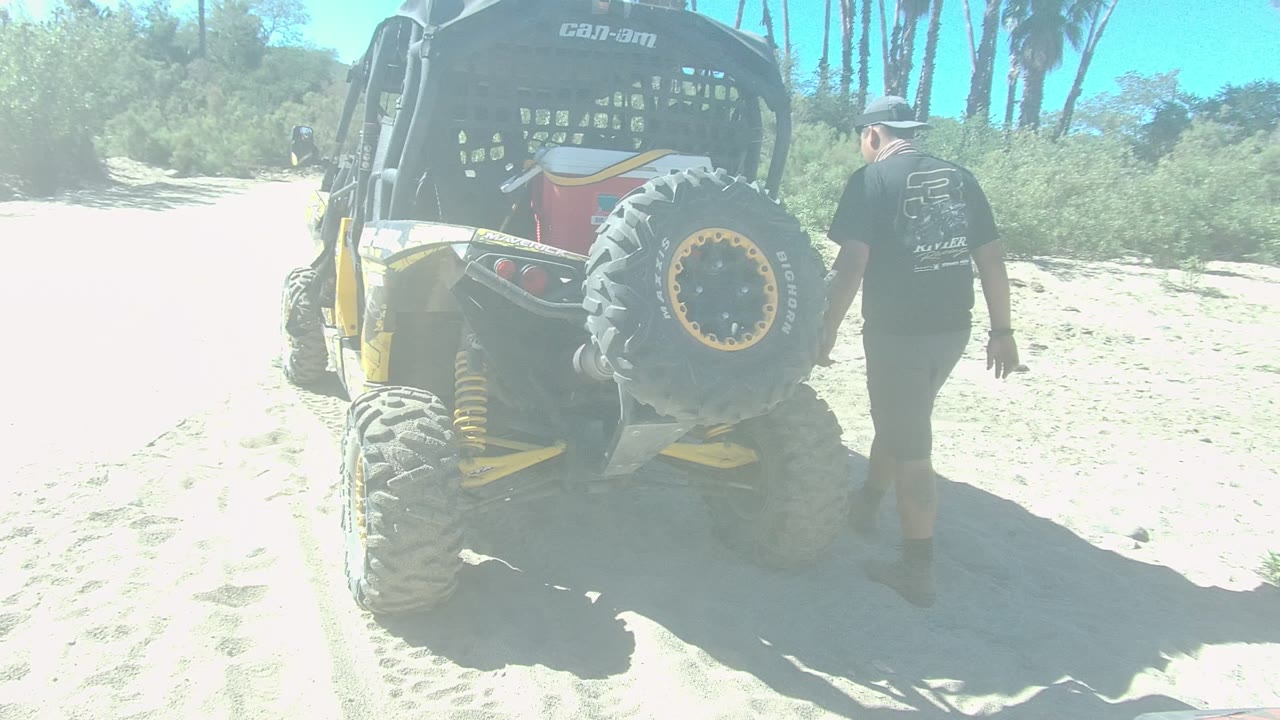 Man walking beside the rear of a dune buggy in bright sand.
