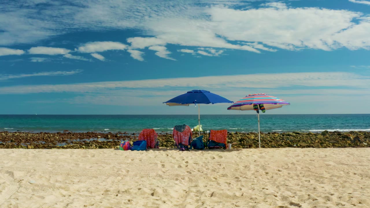 Two umbrellas and empty chairs on a sandy beach with ocean behind